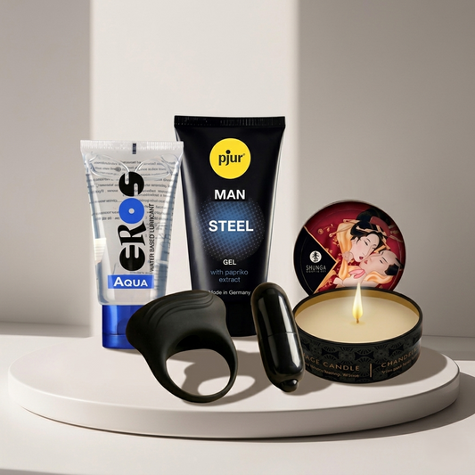 Kit Vencedor Diamora: Fotografia minimalista e luxuosa expondo o gel pjur Steel Booster, o anel duplo preto Bertram, a vela Shunga e o lubrificante EROS Aqua alinhados sobre uma superfície de mármore esbelta.