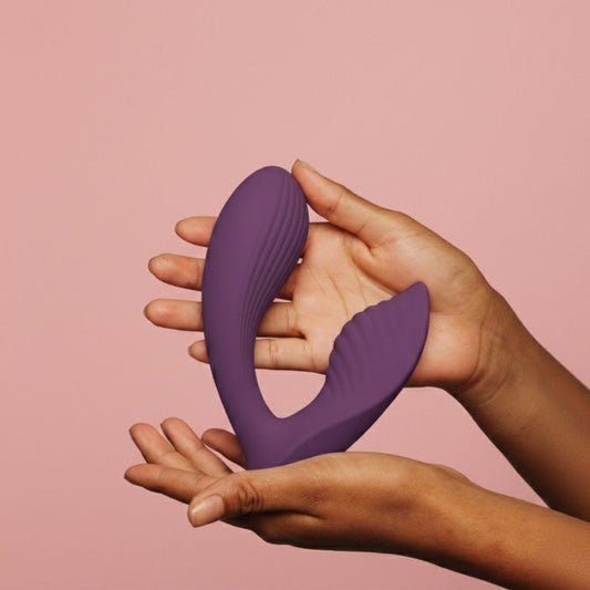 Vibrador Interativo Pretty Love Franz: Fotografia comercial sofisticada em fundo minimalista, focando no vibrador de silicone roxo com acabamento mate, posicionado elegantemente ao lado de um smartphone que exibe a interface da aplicação.